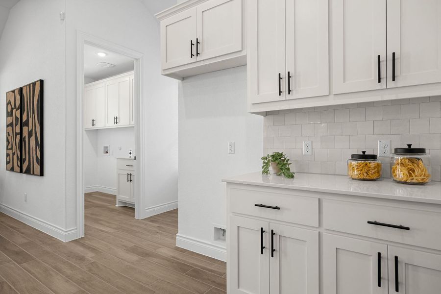 Bar area featuring white cabinets, light wood-type flooring, light stone counters, decorative backsplash, and recessed lighting