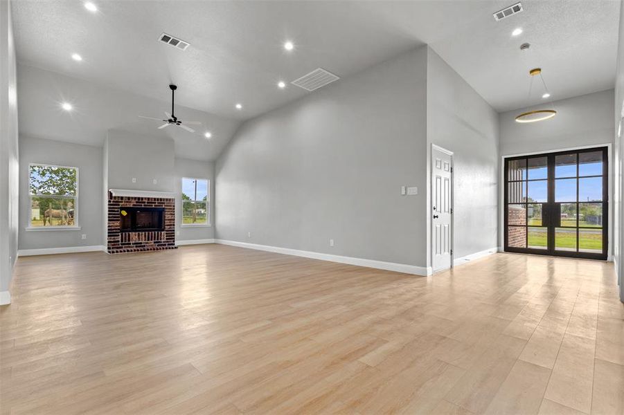 Unfurnished living room with recessed lighting, high vaulted ceiling, light wood-style floors, a ceiling fan, and a brick fireplace