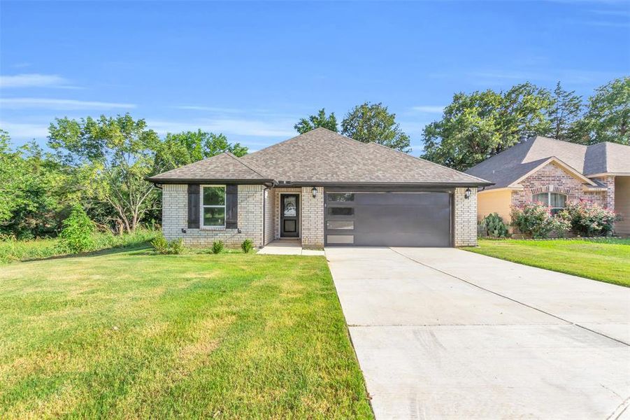 View of front of property featuring driveway, brick siding, a front yard, and an attached garage