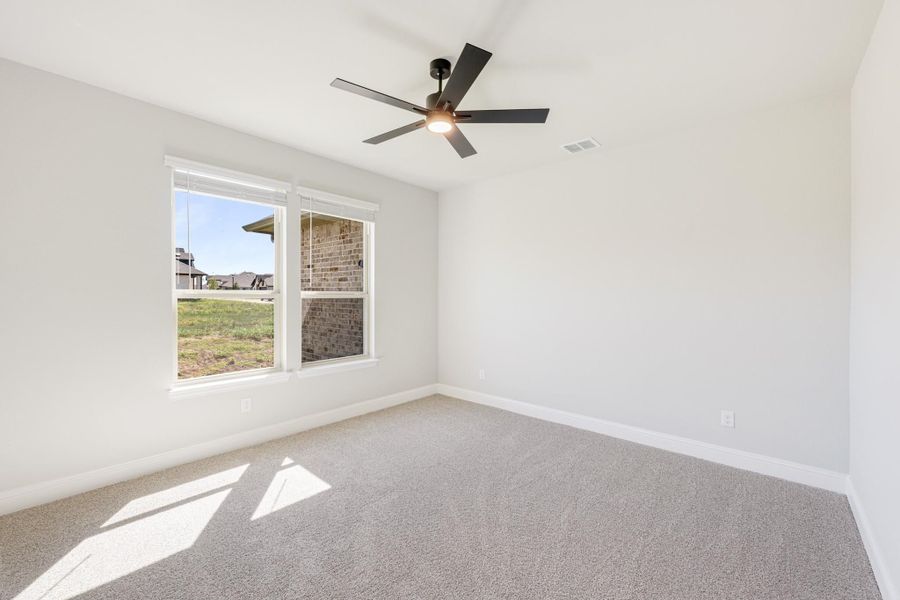 Empty bedroom with vaulted ceiling, ceiling fan, carpet flooring, and a double window with natural light. Empty bedroom with vaulted ceiling, ceiling fan, carpet flooring, and a double window with natural light.