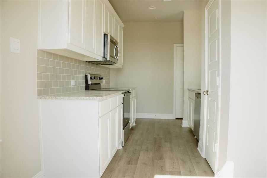 Kitchen featuring white cabinets, decorative backsplash, stainless steel appliances, and light hardwood / wood-style flooring