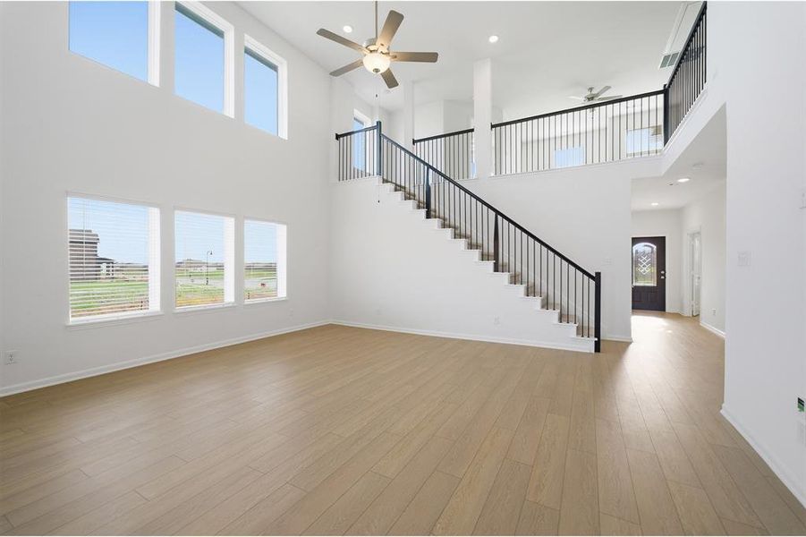 Unfurnished living room featuring ceiling fan, plenty of natural light, a high ceiling, light wood-style flooring, and recessed lighting