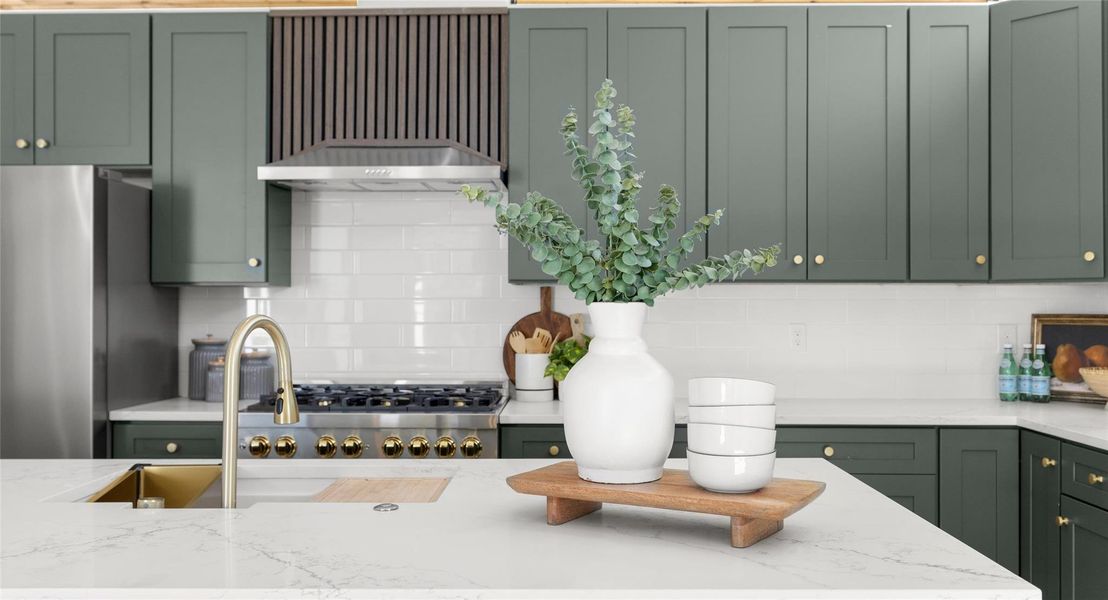 Kitchen featuring green cabinets, light stone counters, stainless steel appliances, and backsplash