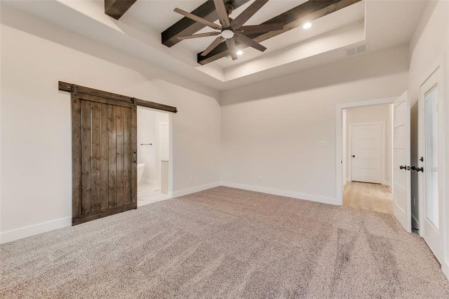 Unfurnished bedroom featuring ensuite bathroom, light carpet, a barn door, ceiling fan, and a tray ceiling Unfurnished bedroom featuring ensuite bathroom, light carpet, a barn door, ceiling fan, and a tray ceiling