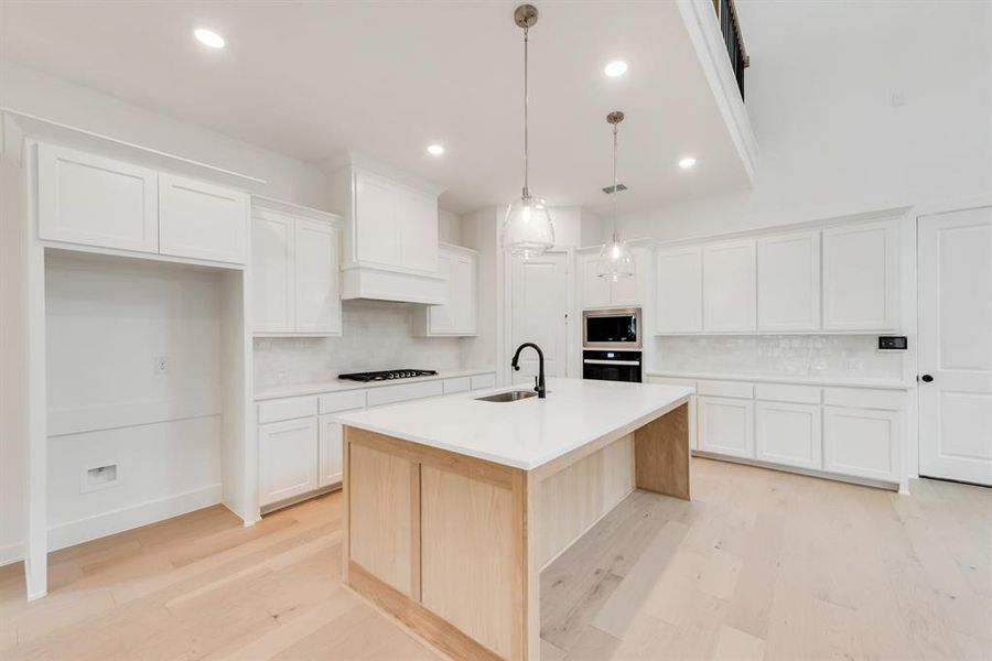 Kitchen featuring tasteful backsplash, light wood-style floors, white cabinets, recessed lighting, and an island with sink Kitchen featuring tasteful backsplash, light wood-style floors, white cabinets, recessed lighting, and an island with sink