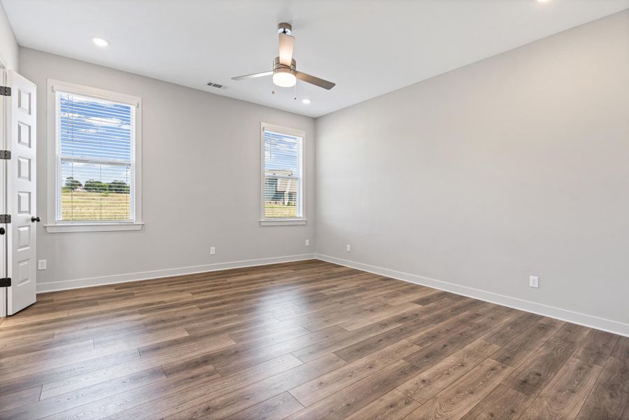 Spacious room featuring wood-finish flooring, two windows with blinds, a ceiling fan, and recessed lighting