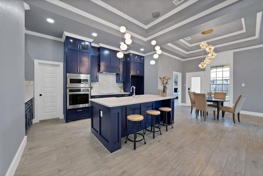 Kitchen and dining area featuring blue cabinetry, stainless steel appliances, a center island with sink, coffered ceilings, and wood-finish flooring