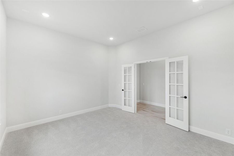 Empty room with gray carpet, white walls, and double French doors with glass panels Empty room with gray carpet, white walls, and double French doors with glass panels