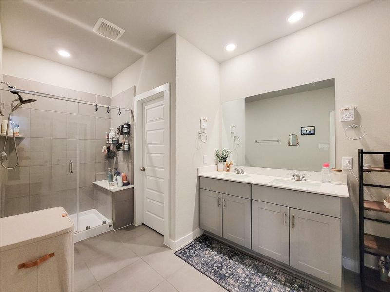 Modern bathroom with a spacious glass-enclosed shower and double vanity. Features sleek tile flooring, ample storage, and recessed lighting for a bright, inviting atmosphere.