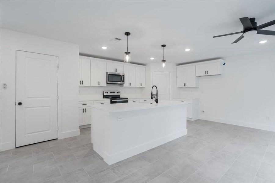 Kitchen featuring white cabinets, appliances with stainless steel finishes, a kitchen island with sink, and ceiling fan