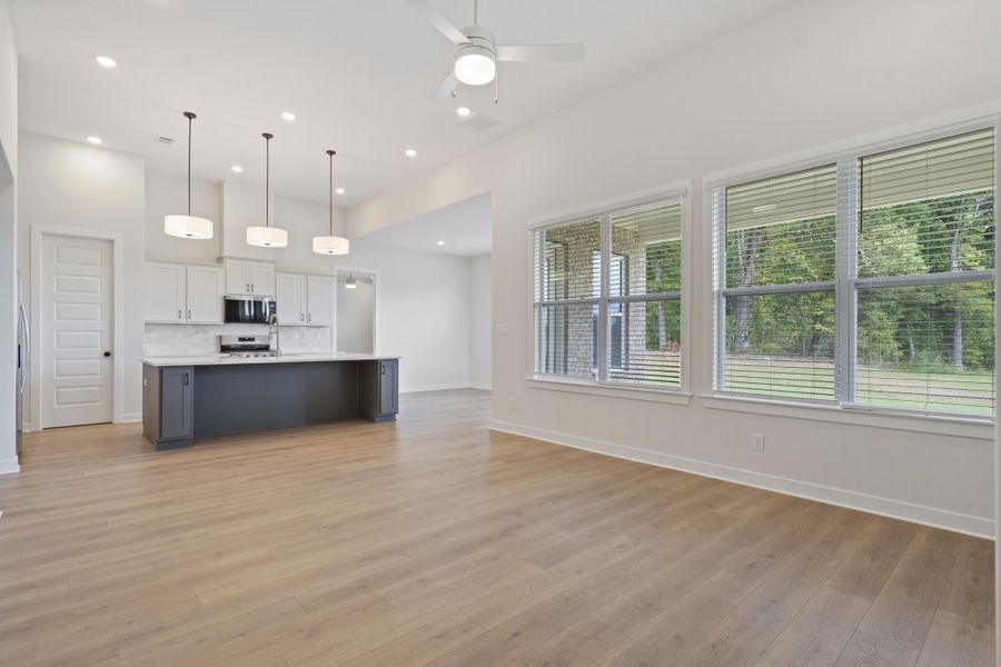 Open-concept living space featuring wood-finish flooring, a kitchen island with seating, stainless steel appliances, and abundant natural light from multiple windows
