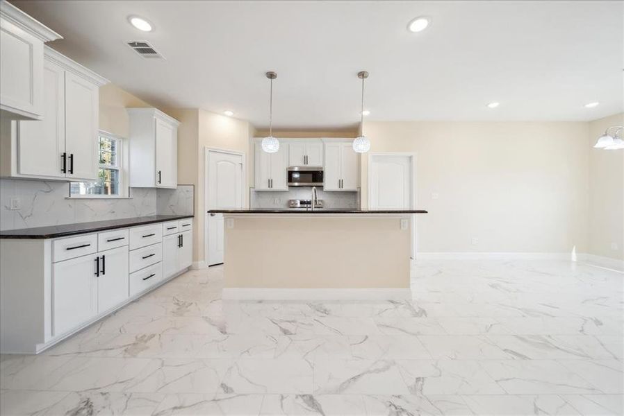 Kitchen featuring pendant lighting, a center island with sink, white cabinetry, and tasteful backsplash