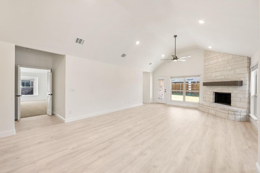 Open living room with vaulted ceiling, stone fireplace, ceiling fan, and light wood floors