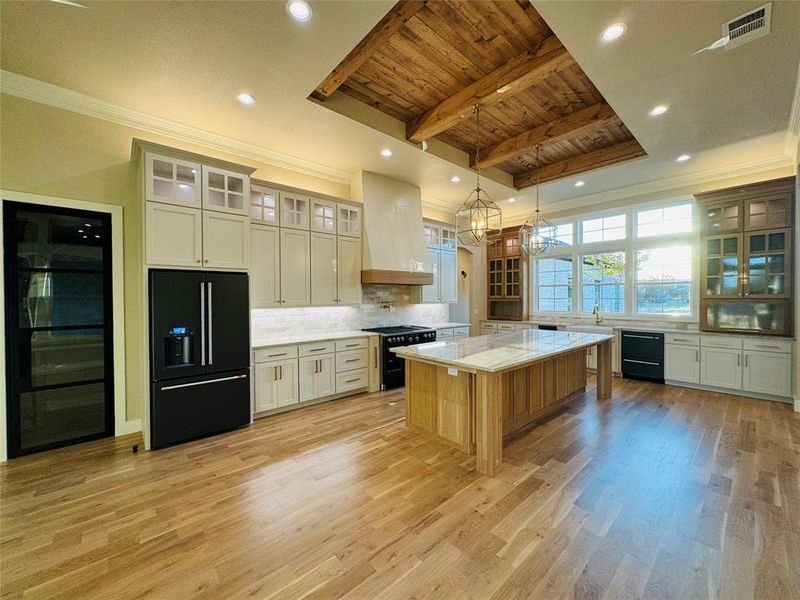 Kitchen with custom exhaust hood, a kitchen island, wooden ceiling, light wood-type flooring, and black appliances