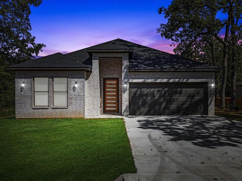View of front of home featuring driveway, brick siding, roof with shingles, a garage, and a lawn