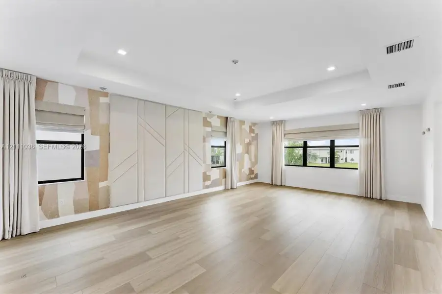 Tray ceiling featuring recessed lighting, light wood-finish flooring, and wall panels with textured geometric detailing