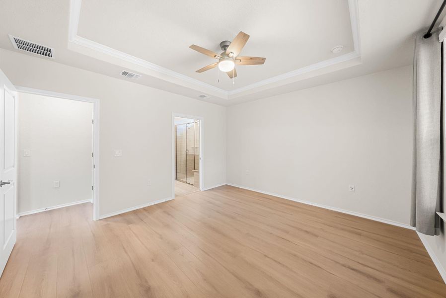A tranquil primary bedroom with light wood flooring and a classic tray ceiling. A tranquil primary bedroom with light wood flooring and a classic tray ceiling.