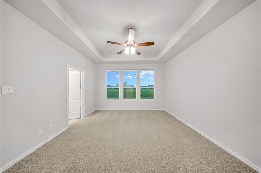 Spare room featuring a tray ceiling, ceiling fan, and light carpet Spare room featuring a tray ceiling, ceiling fan, and light carpet