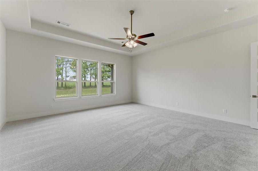 Spacious room featuring light gray carpeting, a tray ceiling, and a ceiling fan with integrated lighting
