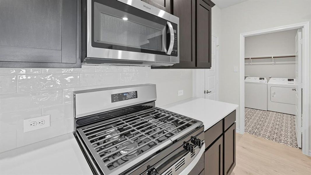 Kitchen featuring stainless steel appliances, light countertops, washing machine and dryer, and light wood-style floors