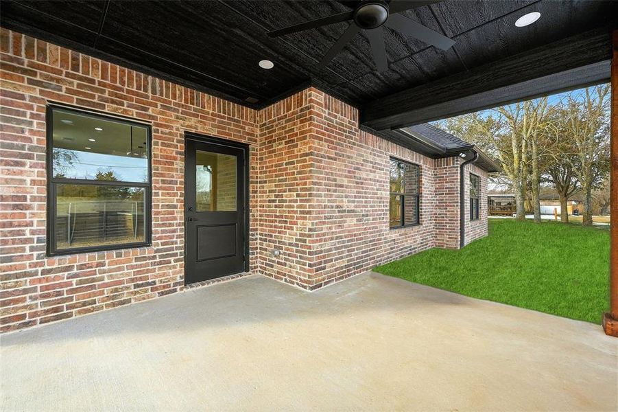 Property entrance featuring a patio, brick siding, ceiling fan, and a lawn Property entrance featuring a patio, brick siding, ceiling fan, and a lawn
