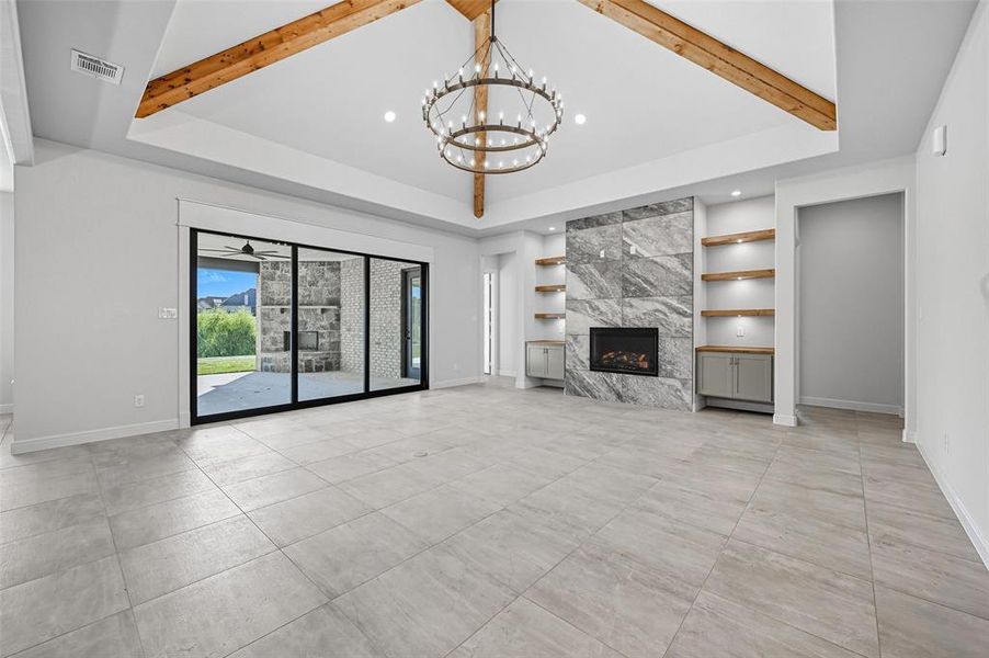 Unfurnished living room with beamed ceiling, built in features, a fireplace, and a chandelier Unfurnished living room with beamed ceiling, built in features, a fireplace, and a chandelier