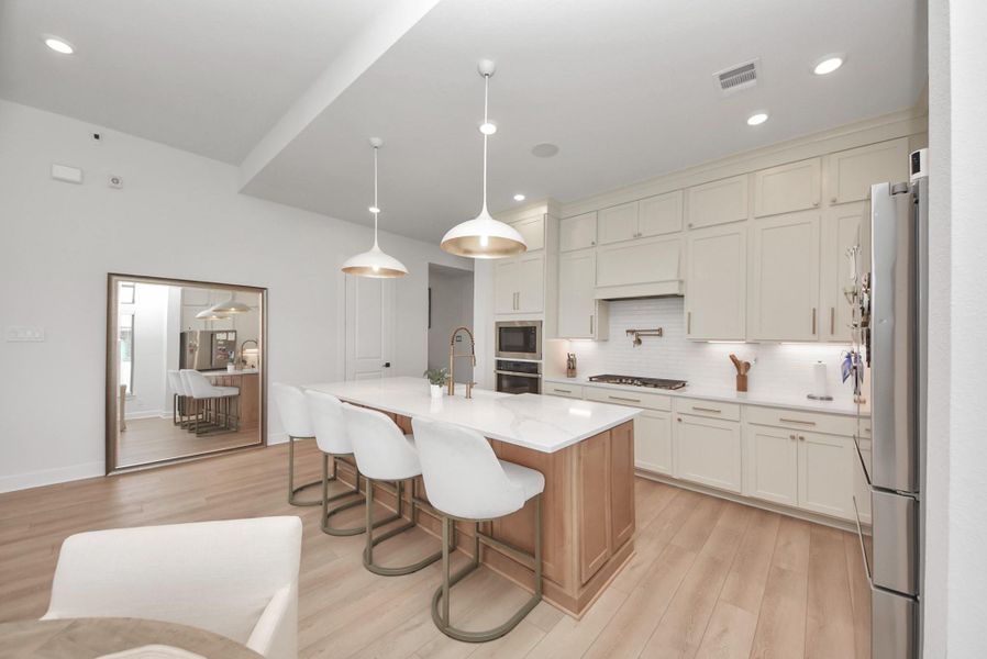 Elegant kitchen featuring a spacious island with sleek countertops, modern pendant lighting, and ample cabinetry, complemented by stainless steel appliances and warm wood flooring.
