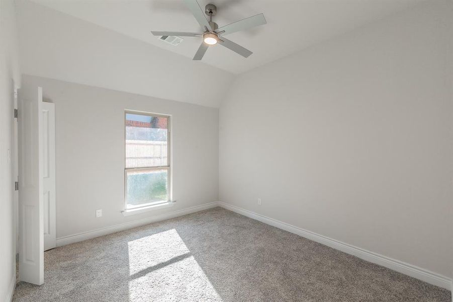 Empty room with light carpet, ceiling fan, and vaulted ceiling