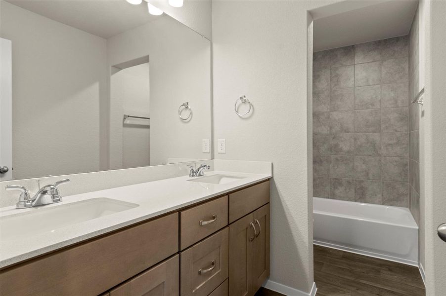 Full bathroom with wood finished floors, double vanity, and washtub / shower combination