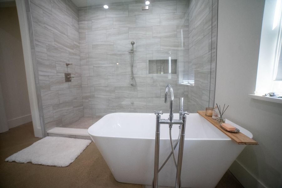This bathroom features a modern freestanding bathtub with sleek, floor-mounted fixtures, serving as the room's sculptural centerpiece. Designed for the ultimate soaking experience, this deep-profile tub offers a spa-like sanctuary for relaxationenclosed shower. The space is accented with light gray tiles and bright natural lighting, creating a serene and elegant atmosphere.