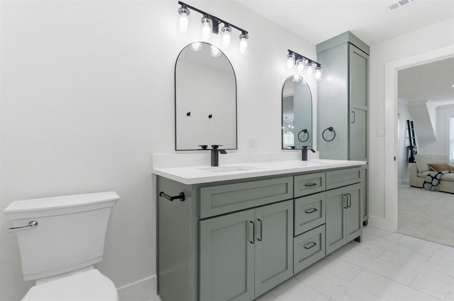 Bathroom featuring a dual vanity with sage green cabinetry, a white countertop, and two arched mirrors with contemporary light fixtures Bathroom featuring a dual vanity with sage green cabinetry, a white countertop, and two arched mirrors with contemporary light fixtures