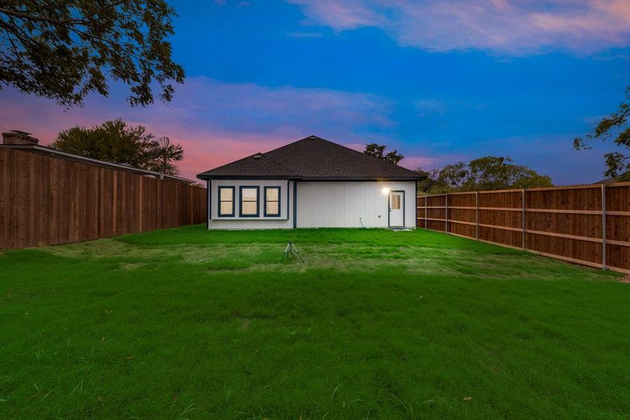 Back house at dusk featuring a yard