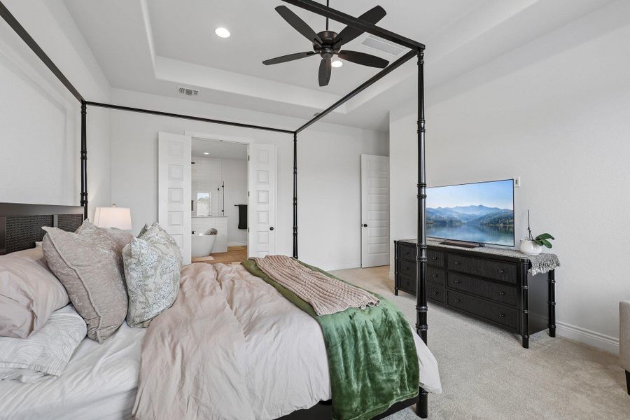 Spacious bedroom featuring a tray ceiling with recessed lighting and a ceiling fan
