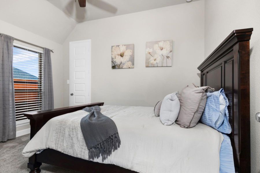 One of four bedrooms featuring a cozy atmosphere with neutral tones, and soft lighting. Large windows with elegant curtains provide ample natural light, while floral artwork adds a touch of sophistication.