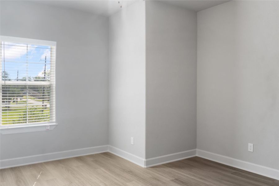 Bright room with light gray walls, a large window with blinds, and wood-like flooring. Ideal for a small office or cozy nook.