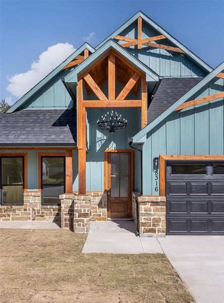 Property entrance with an attached garage, roof with shingles, and stone siding