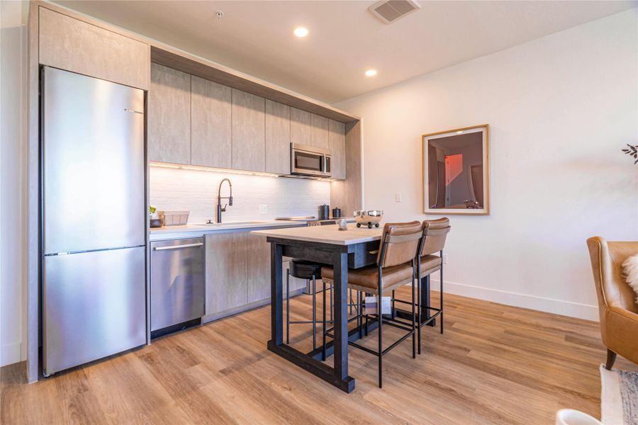 Kitchen featuring stainless steel appliances, modern cabinets, light wood finished floors, backsplash, and light wood finish cabinetry.Photos shown are of a model residence and are representative in nature. Actual residence may differ in layout, finishes, and views.