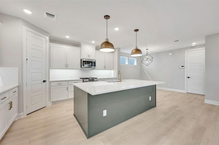 Kitchen featuring a kitchen island with sink, pendant lighting, stainless steel appliances, light wood-style flooring, and two tone color scheme