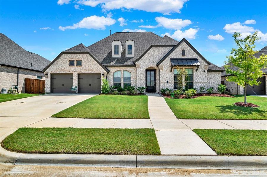 French country inspired facade featuring brick siding, a shingled roof, and driveway French country inspired facade featuring brick siding, a shingled roof, and driveway