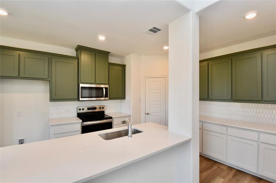 Kitchen featuring green cabinets, appliances with stainless steel finishes, backsplash, light stone counters, and light wood-style floors