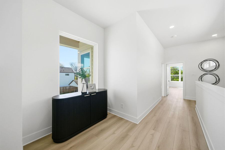 This photo showcases a bright, modern hallway with light wood flooring and white walls. It features an additional nook area for lounging or a desk.