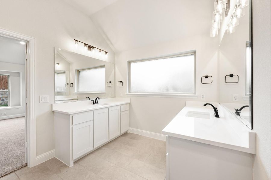 Bathroom with dual vanities, white cabinets, black fixtures, and vaulted ceiling with tile floors Bathroom with dual vanities, white cabinets, black fixtures, and vaulted ceiling with tile floors