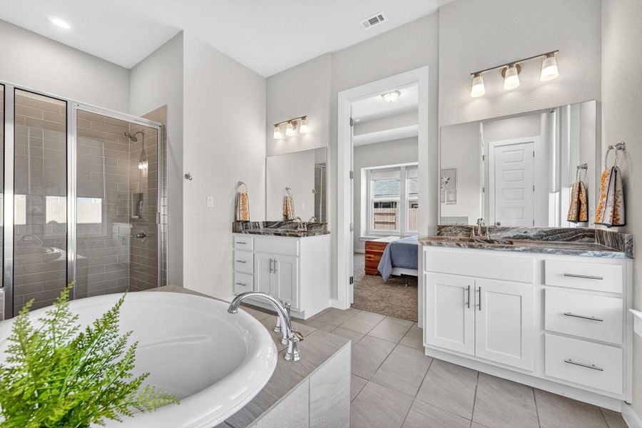Primary bath with two vanities, a bath, a walk-in shower, ensuite bathroom, and light tile floors. There's also an oversized walk-in closet.