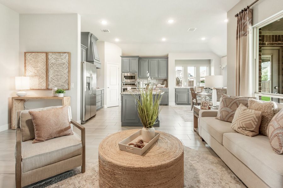 Open-concept living room with neutral furnishings flowing into kitchen with gray cabinets and island