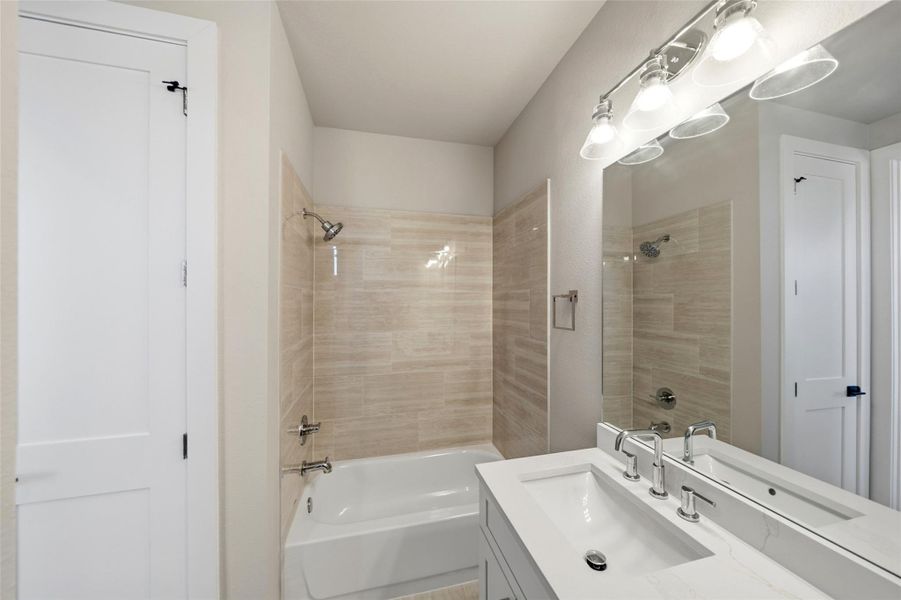 This bathroom features a modern design with neutral tones, a sleek vanity with dual sinks, a large mirror, and a bathtub with textured tile walls. Bright lighting enhances the clean, spacious feel.