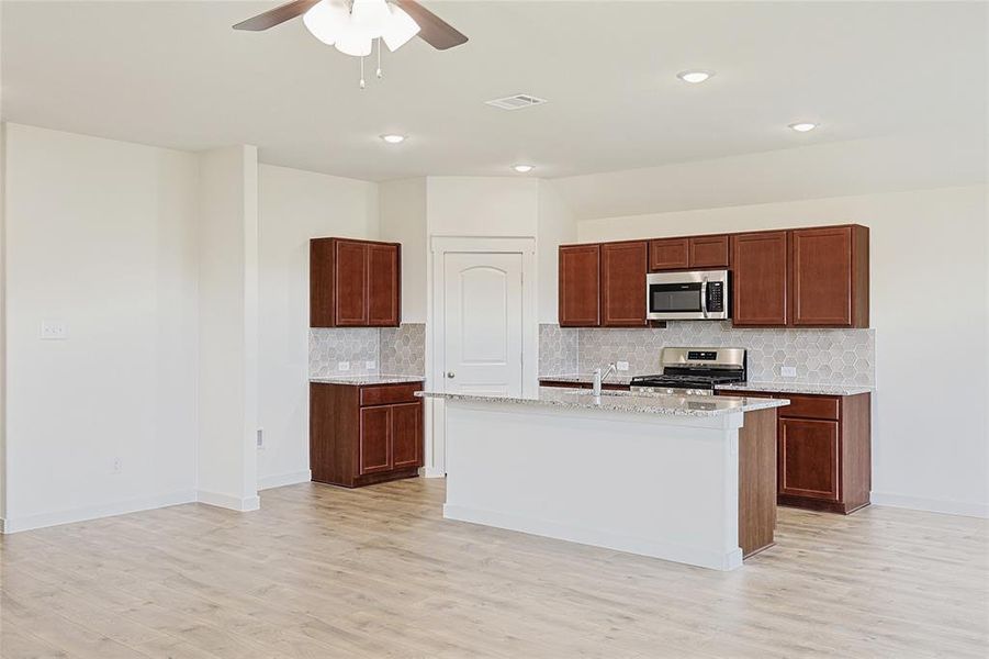 Kitchen with backsplash, a kitchen island with sink, ceiling fan, light hardwood / wood-style floors, and stainless steel appliances