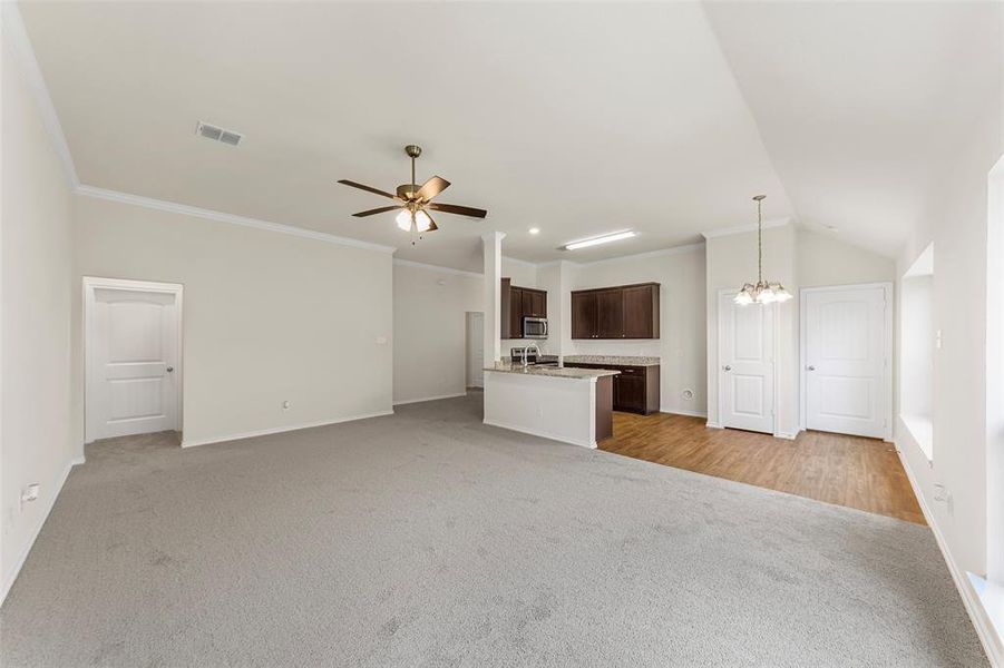 Unfurnished living room with light carpet, baseboards, a chandelier, crown molding, and ceiling fan Unfurnished living room with light carpet, baseboards, a chandelier, crown molding, and ceiling fan