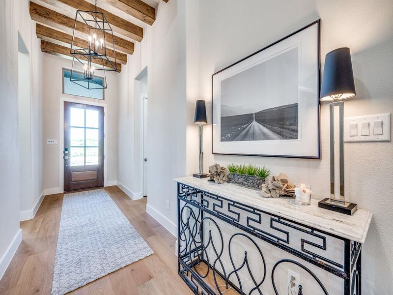 Entryway featuring beamed ceiling, light wood-style flooring, a chandelier, and baseboards