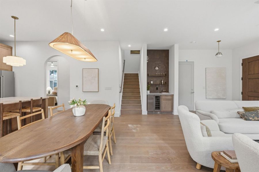 An open-concept living area features warm wood flooring, a central dining table, and a dedicated beverage station.