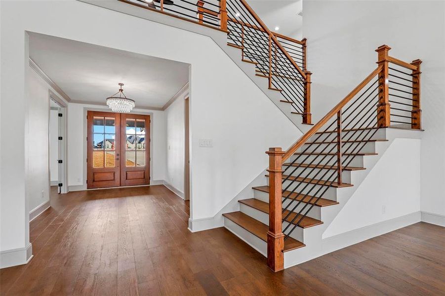 Entrance foyer featuring dark wood-type flooring, french doors, a chandelier, ornamental molding, and a towering ceiling